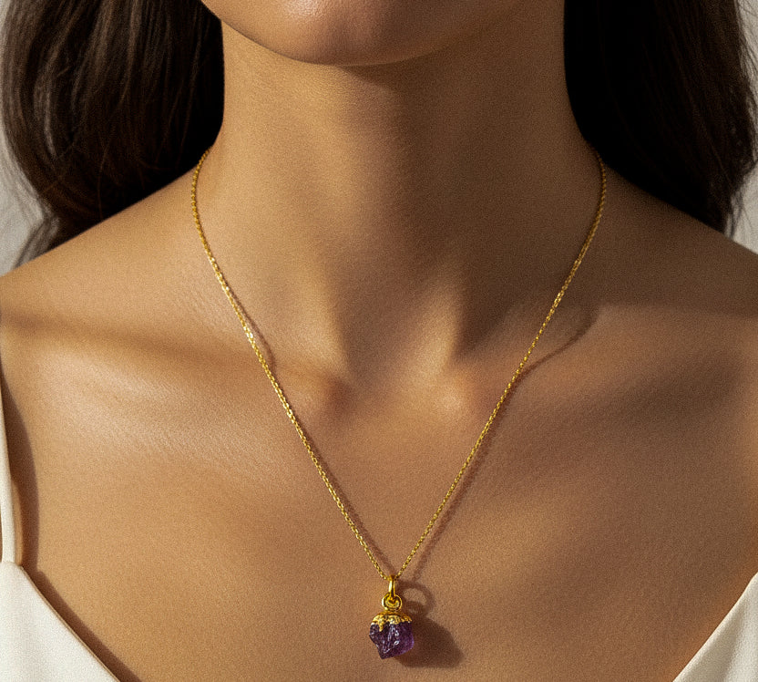 Close-up of a woman wearing a gold necklace with a purple Amethyst pendant.