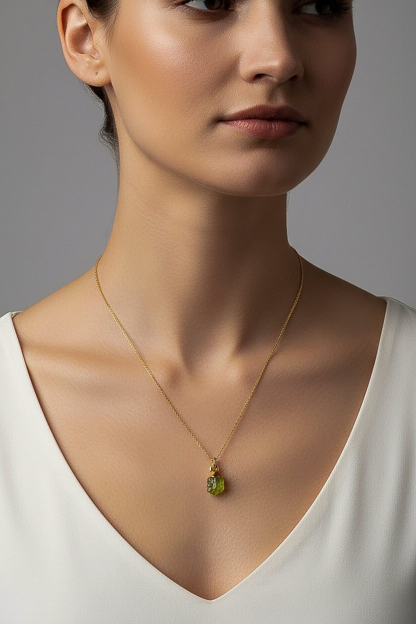 Woman wearing a gold necklace with a green peridot pendant against a neutral background