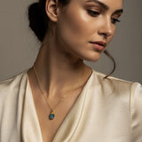 Woman wearing a gold necklace with a raw Turquoise crystal pendant against a neutral background